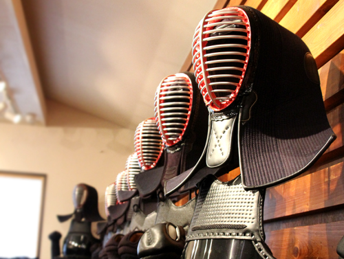 Kendo protective head gear, breastplate, and gauntlet displayed on stands lined up against a wall